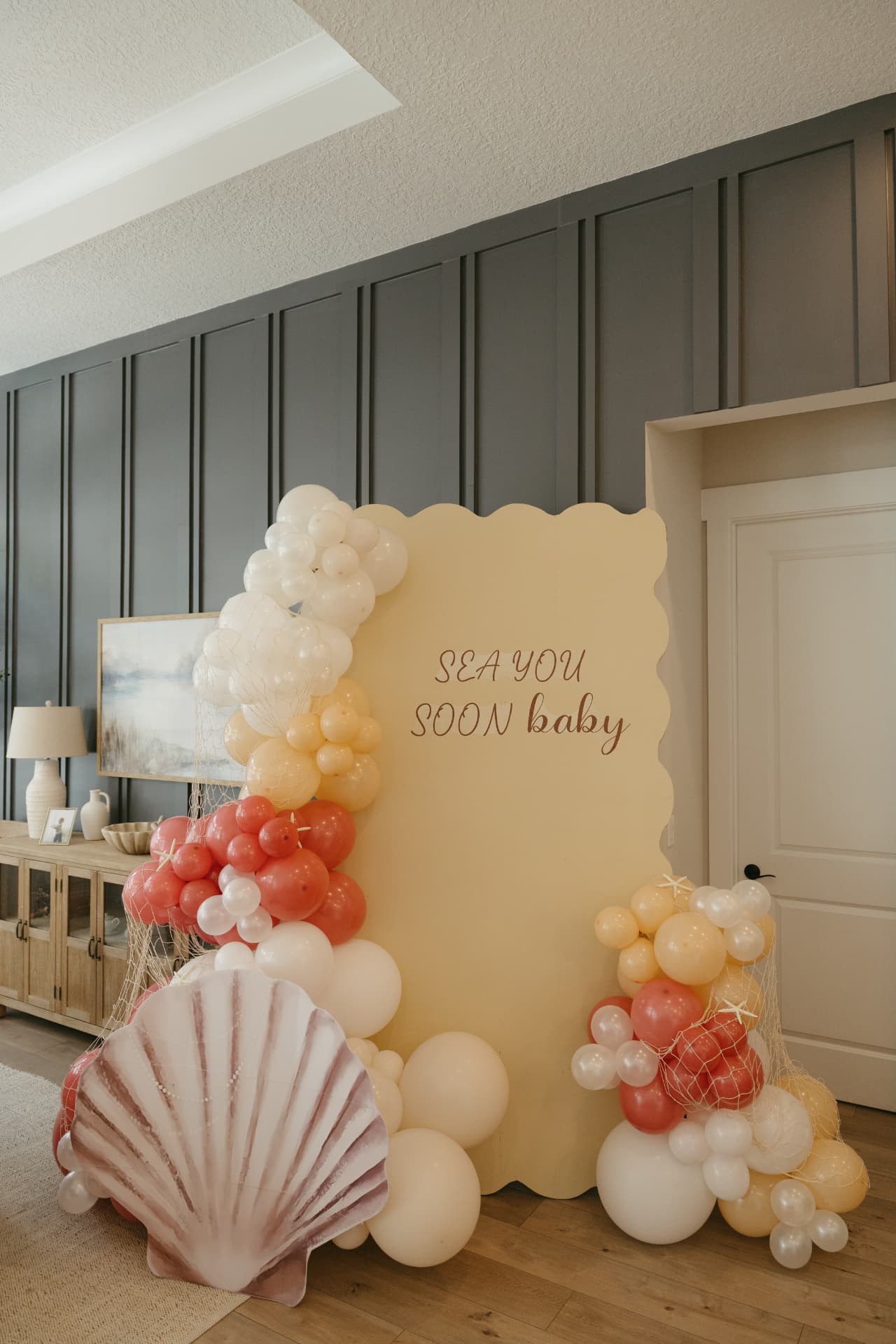 Nautical baby shower themed build with scalloped backdrop, seashell prop and coral, cream and white balloon garlands
